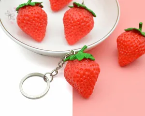 Detailed close-up of realistic red PVC strawberry keychains with green leaves