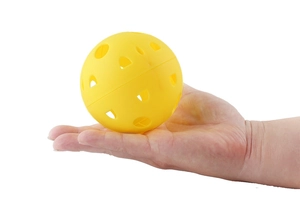 Close-up of a large yellow perforated pickleball being held to show size and texture