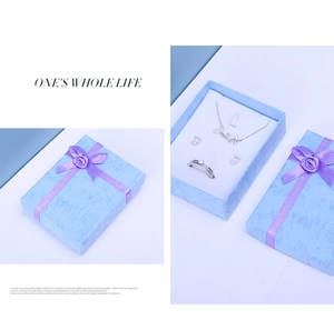 Detail of blue textured jewelry gift box with purple ribbon, necklace, earrings and ring