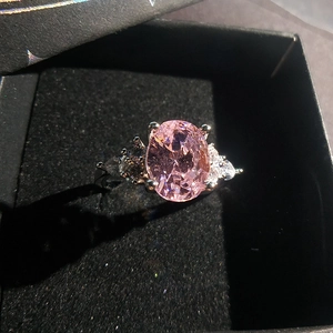 Close-up of pink oval gemstone ring with pear-cut side diamonds in a black velvet gift box