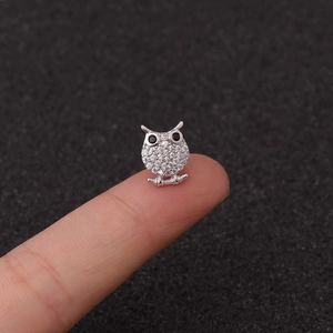 Macro shot of silver owl cartilage stud earring with cubic zirconia on a fingertip