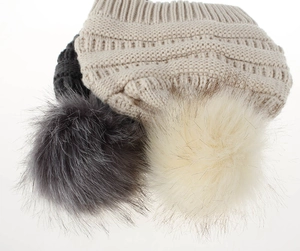 Nahaufnahme der dicken Strickstruktur und flauschigen Kunstpelz-Pompons an Wintermützen