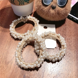 Detailed view of three pearl beaded hair ties displayed on a rustic wooden table surface
