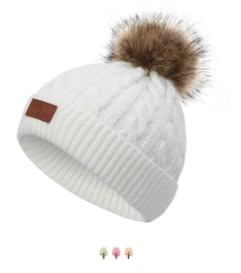 Détail du bonnet en maille torsadée blanc crème avec pompon en fausse fourrure brune