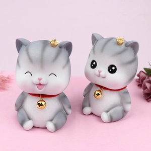 Detail of grey striped resin cat figurines with gold crowns and bells on pink background