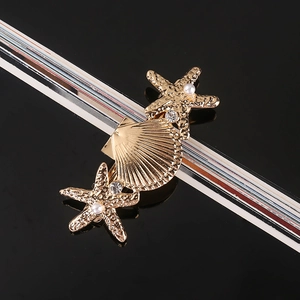 Detail of a gold starfish and shell hair clip with pearls and rhinestones on black background