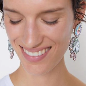 Macro detail of large rhinestone skeleton drop earrings worn to show scale and sparkle