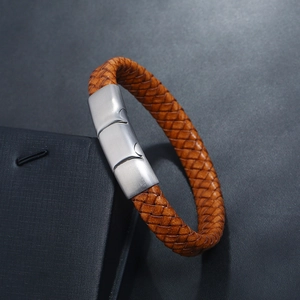 Brown braided leather bracelet with brushed silver magnetic clasp on a textured display box