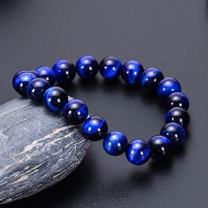 Natural blue tiger eye stone bracelet with shimmering beads on a gray textured rock