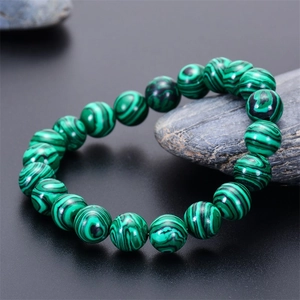 Detailed view of natural green malachite beaded bracelet on a dark stone background