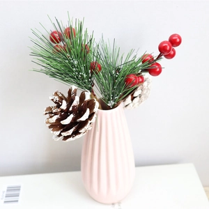 Artificial Christmas tree branches with red berries and pine cones in pink ceramic vase