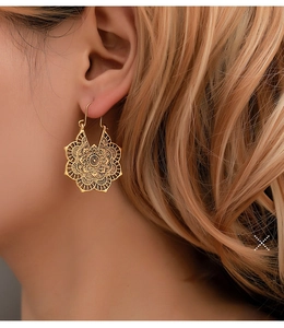 Détail de boucles d'oreilles fleurs ajourées dorées avec motifs bohèmes gravés