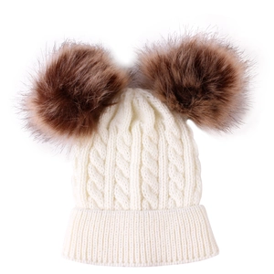 Detail of baby knitted hat with twin brown pom-poms and white cable knit texture