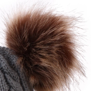 Close-up of cable knit texture and fluffy brown pom-poms on gray knitted baby hat