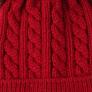 Macro detail of red cable knit pattern on thick winter hat showing warm wool texture
