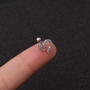 Macro view of a heart-shaped silver ear stud with sparkling clear zircon stones on a fingertip