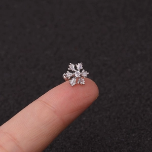 Detailed view of a small silver snowflake ear stud with zircon on a fingertip