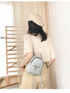 Model wearing a light grey mini leather backpack with gold zippers in a cozy home setting