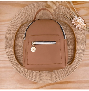 Top view of a brown PU leather mini backpack on a woven mat with shell decorations