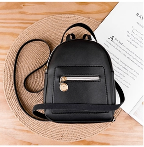 Overhead view of a black mini backpack on a straw mat with an open magazine
