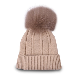 Close-up of beige knit beanie featuring thick vertical ribbing and a large faux fur pom-pom