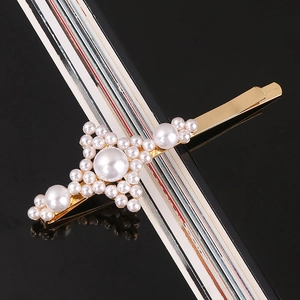 Close-up of golden alloy hair clip with white pearls on a sleek black background
