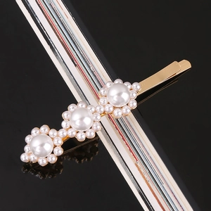 Detail of gold bobby pin with three pearl flowers on a reflective black surface