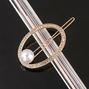Macro shot of a vintage gold oval hair clip with sparkling rhinestones and a large pearl