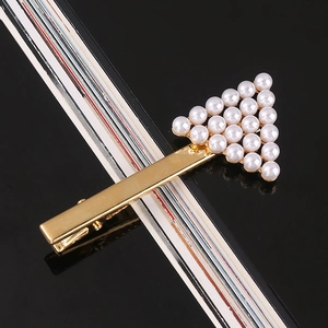 Detail shot of a golden alloy hair clip featuring a triangular faux pearl arrangement