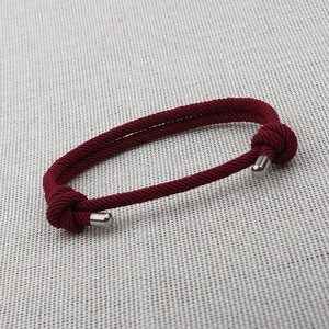 Detail of red nylon rope bracelet with silver metal ends and large knots on fabric