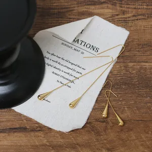 Detail of 18K gold-plated teardrop earrings on white linen over a wooden surface