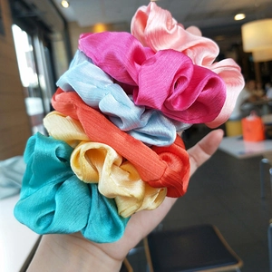 Colorful satin silk scrunchies set held in hand featuring glossy vibrant fabric texture