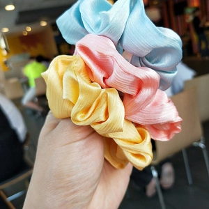 Three pleated satin hair scrunchies in yellow, pink, and blue with a silky texture