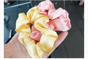 Detailed close-up showing light pink and bright yellow satin fabric hair scrunchies