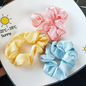 Three-piece set of satin hair scrunchies in pink, yellow, and blue with silky wavy texture