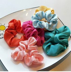 Macro detail of multi-color pleated satin hair scrunchies with soft silk luster texture