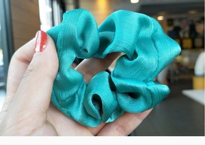 Close-up of a blue satin silk scrunchie with smooth texture and soft pleated fabric detail