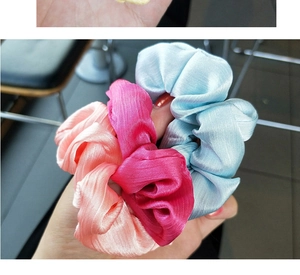 Close-up of three satin scrunchies in pink, rose and light blue with a soft silky texture