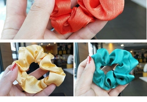 Detailed texture of shiny satin scrunchies in orange, pale yellow, and teal fabric