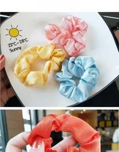 Detail view of satin hair scrunchies in pastel colors on a white decorative dish