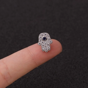 Macro view of silver Hamsa hand stud earring with blue stone held between fingers