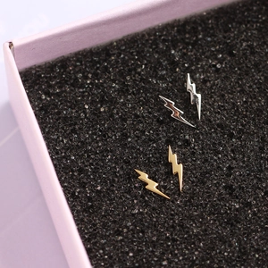 Detailed view of minimalist gold and silver lightning bolt stud earrings in a box