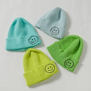 Kids knitted beanie hats with smiley faces in light blue, green, and yellow tones