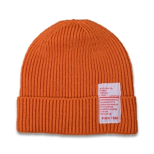 Detail of orange ribbed knit baby beanie featuring a white woven patch with text
