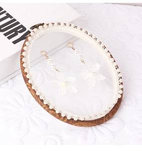 Detail of white lace flower earrings with pearls on a vintage embroidery frame stand