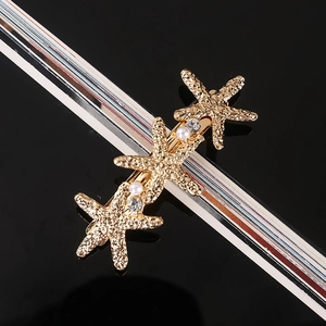 Detailed close-up of golden starfish hair clip with pearls and rhinestones on black surface