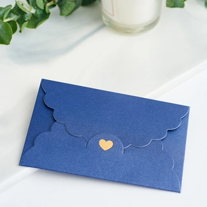 Mini blue pearlescent envelope with gold heart sticker on white marble tabletop