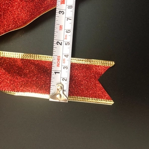 Detail showing red and gold glitter Christmas ribbon width measured at 1.5 inches