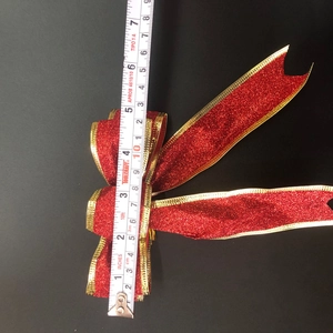 Close-up of a red glitter Christmas bow with gold trim being measured by a tape tool