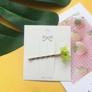Detail shot of a yellow-green acrylic gummy bear hair clip on a branded white paper card